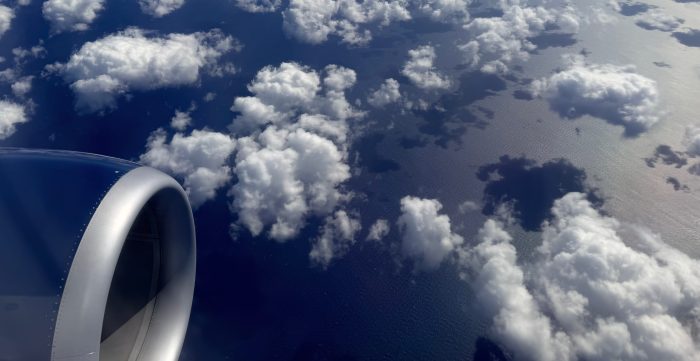 An airplane flies above the gulf with clouds shown below.